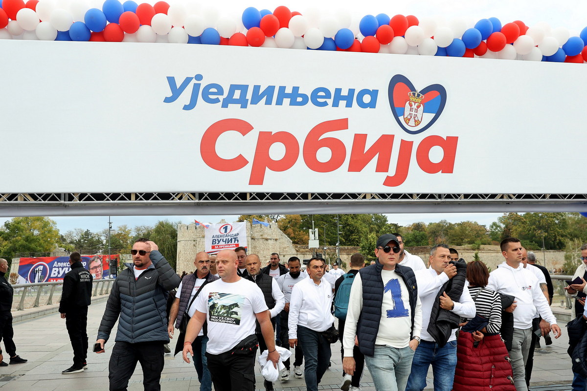 People walk past a campaign banner reading "United Serbia" ahead of the SNS party's campaign rally in Niš.